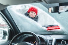 A smiling woman scraping snow from a car windshield