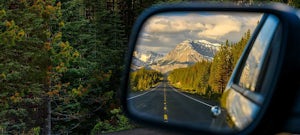 Side mirror of a moving car offers a picturesque view of the mountains of Alberta
