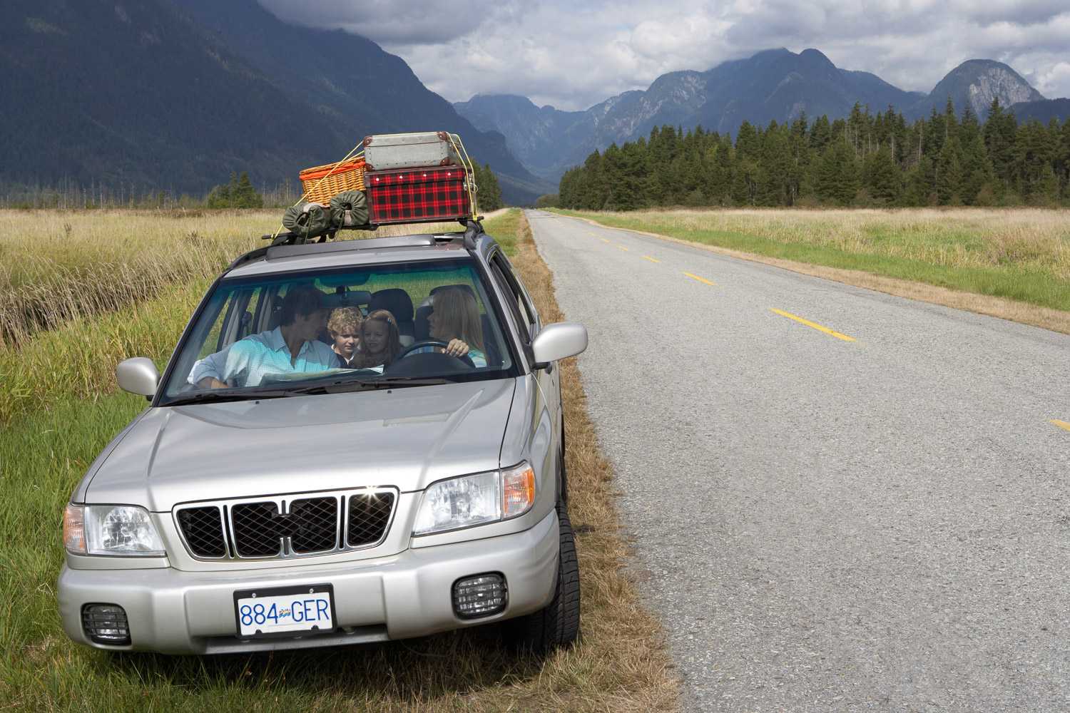 A vehicle is pulled over on the side of the road with two occupants and luggage placed on the hood.