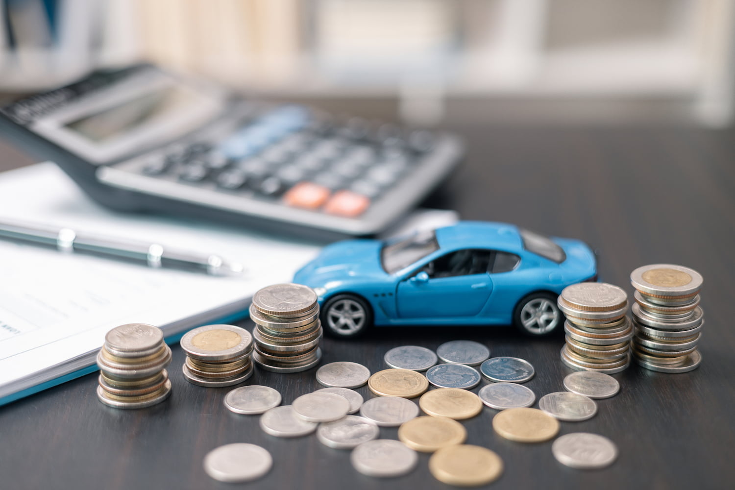 Desk scene featuring a car model, coins, pen, and notepad.