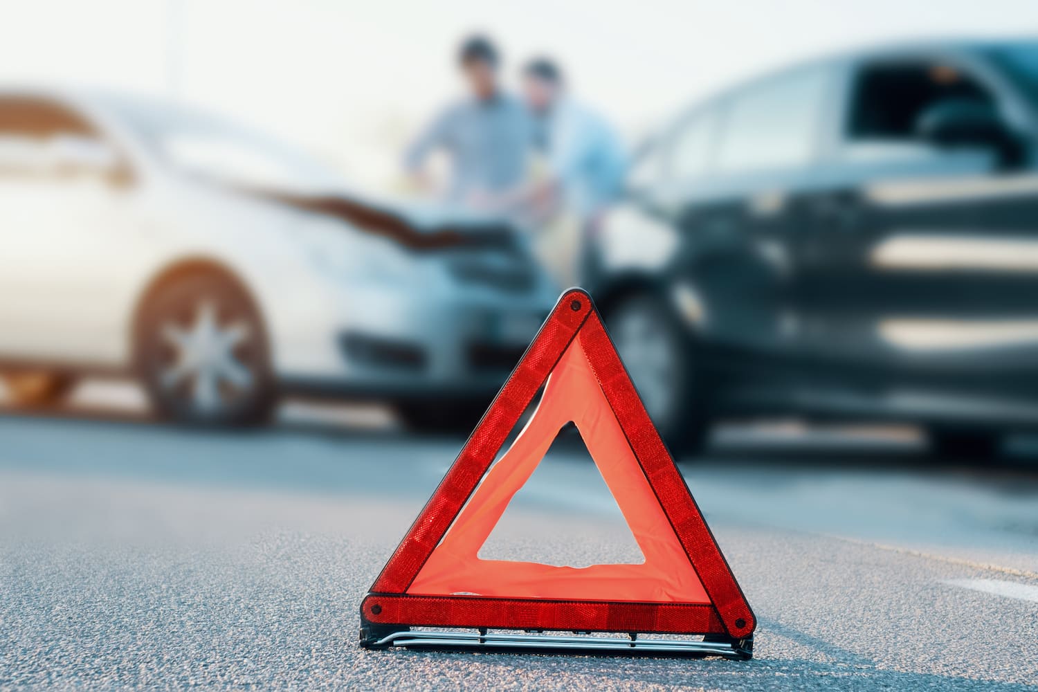 Red emergency triangle on the road with the blurred background of two cars and drivers involved in an accident