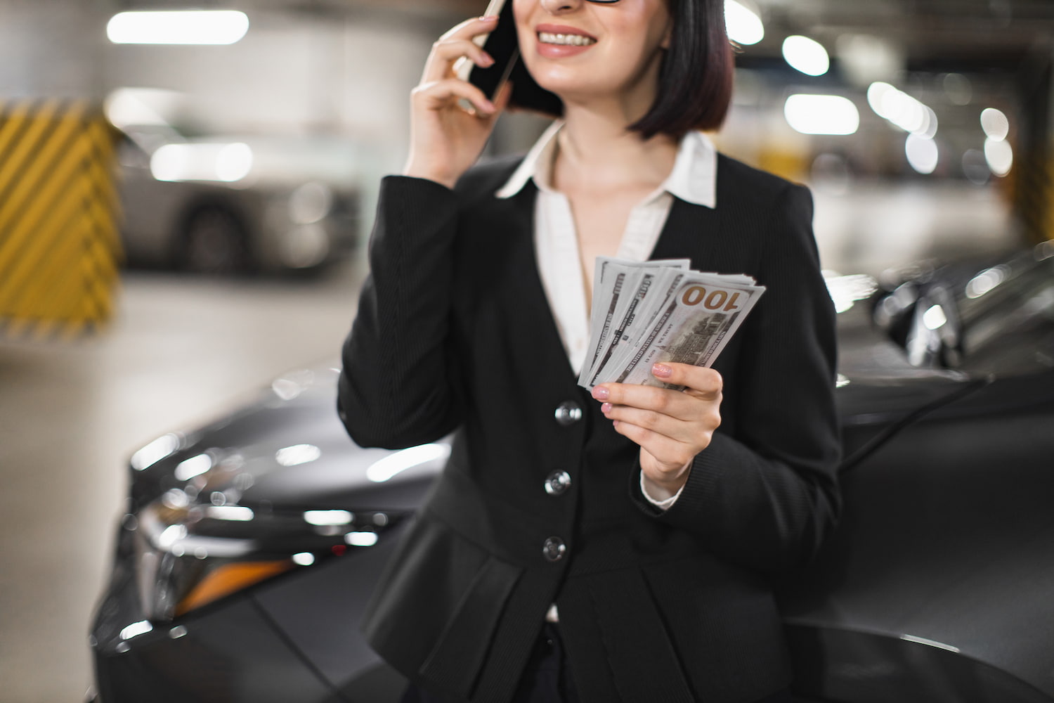 Individual on a phone call, holding cash, in a covered parking area.