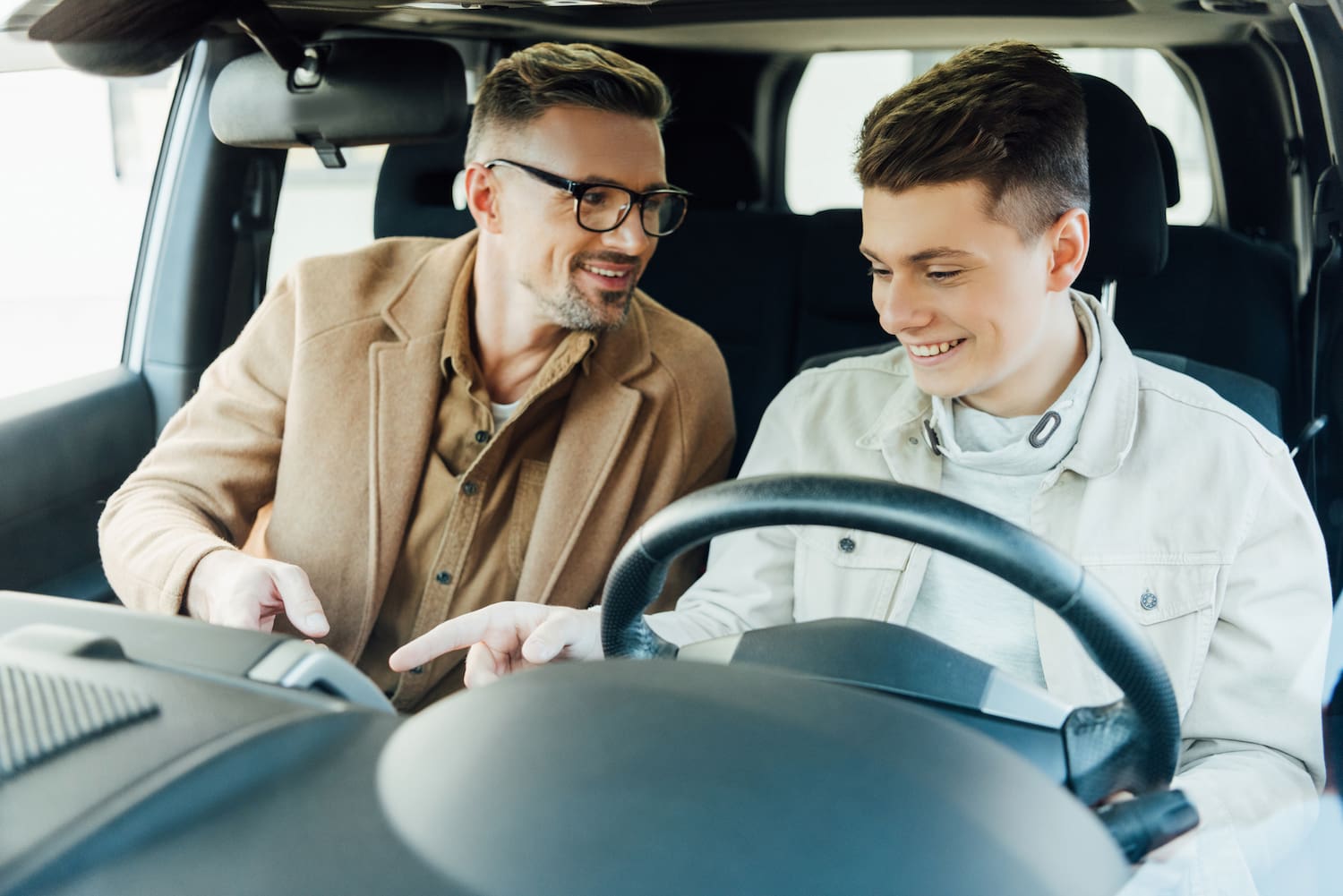 A teenage boy sitting behind the steering wheel of a car and listening to his fathers instructions