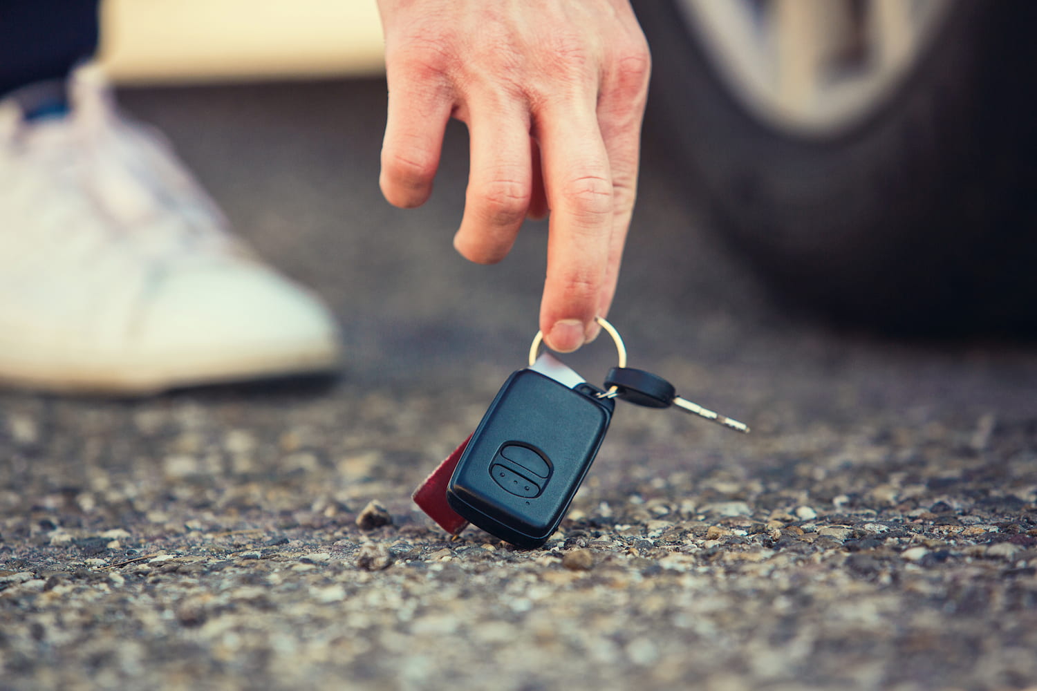 Close up of person hand lifting car keys fallen on the ground.