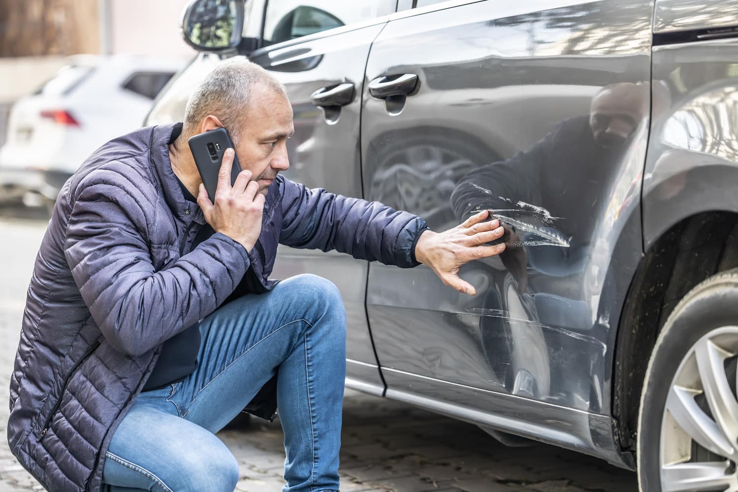 A person is on the phone after their parked car is damaged by another vehicle.
