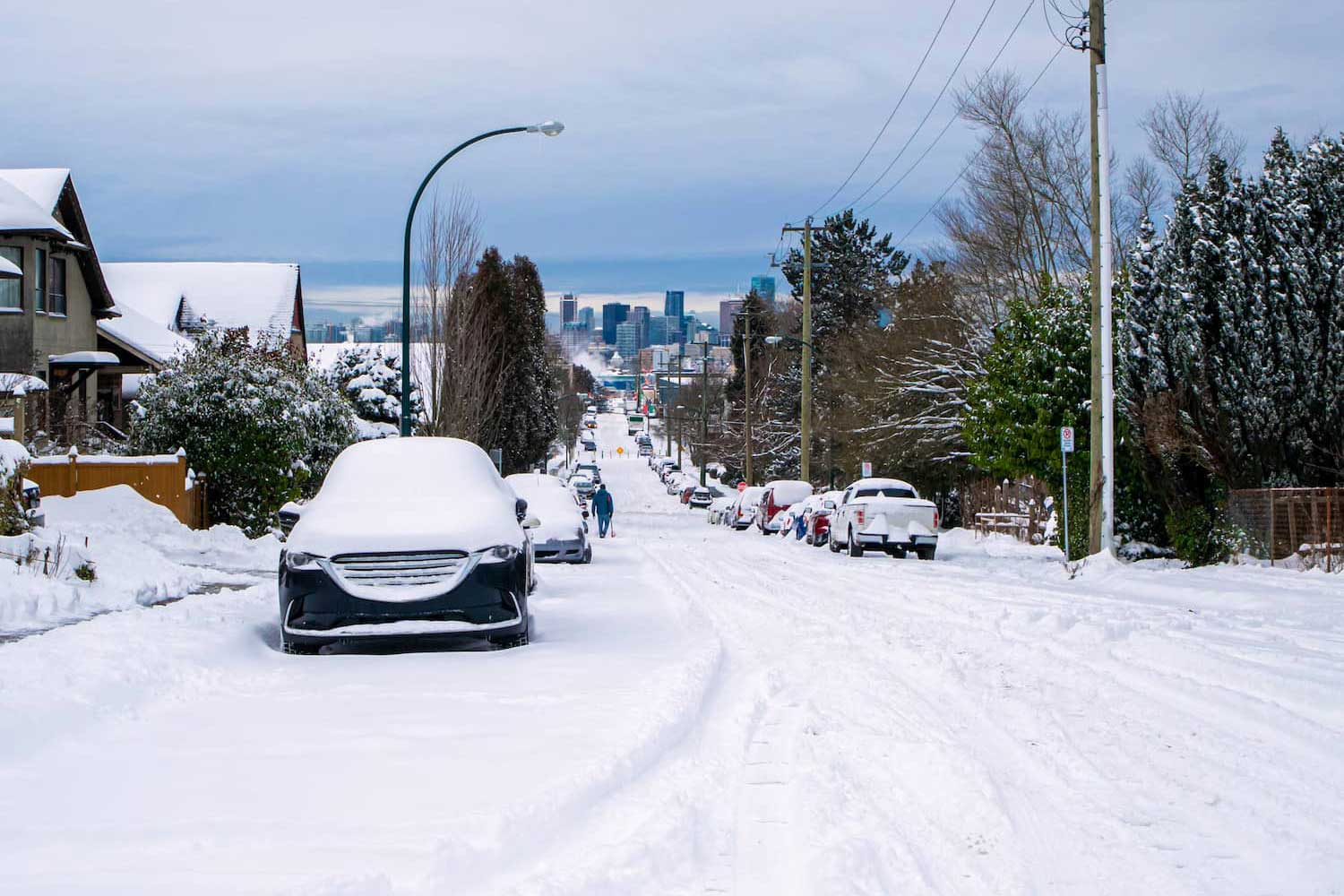 A street in Vancouver, British Columbia, Canada, it's not plowed and many parked cars covered with snow.