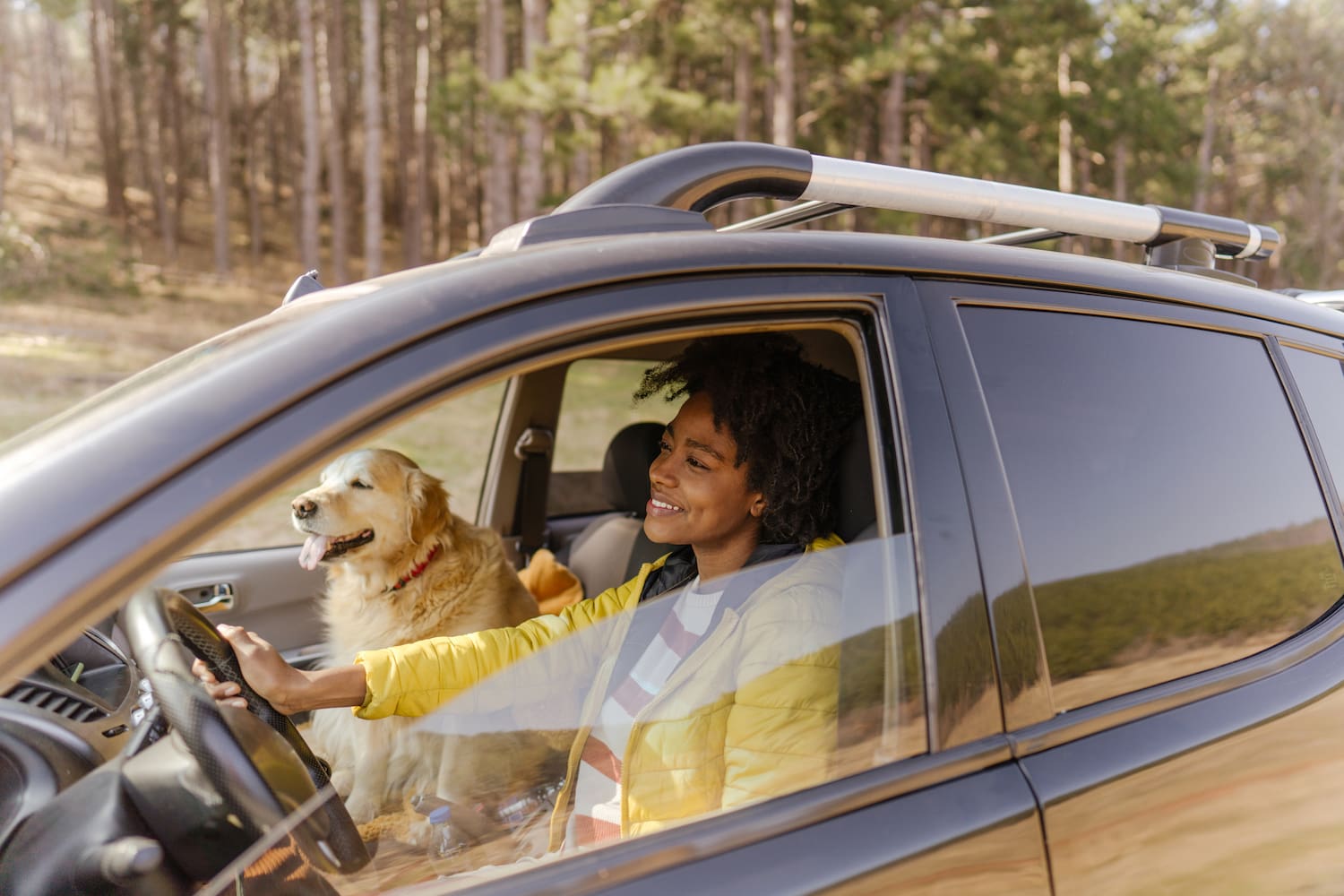 A woman driving a car with her dog in the passenger seat, both looking happy