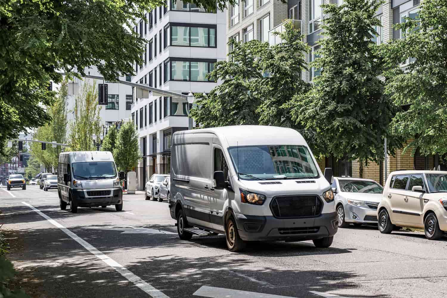 Commercial cargo vans making deliveries on a city street lined with multilevel buildings.