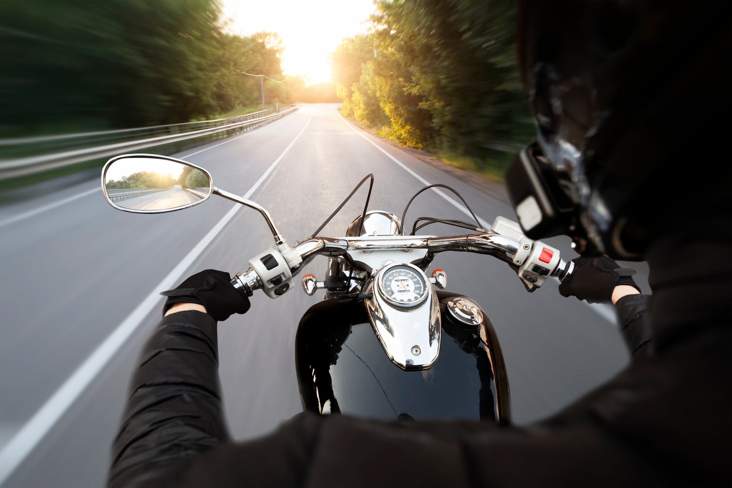 The motorcyclist is riding through the empty asphalt road in the evening.