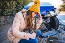 oung frustrated woman crouches next to wrecked car after a car accident