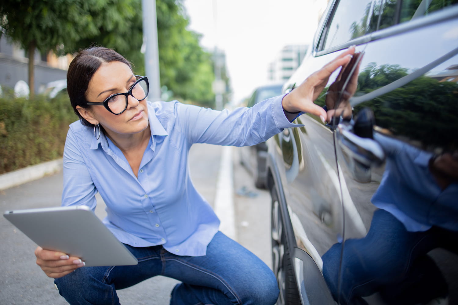 An individual examining a car while taking notes on a clipboard.