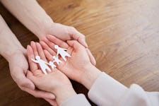 Male and female hands holding family paper model on wooden tabletop