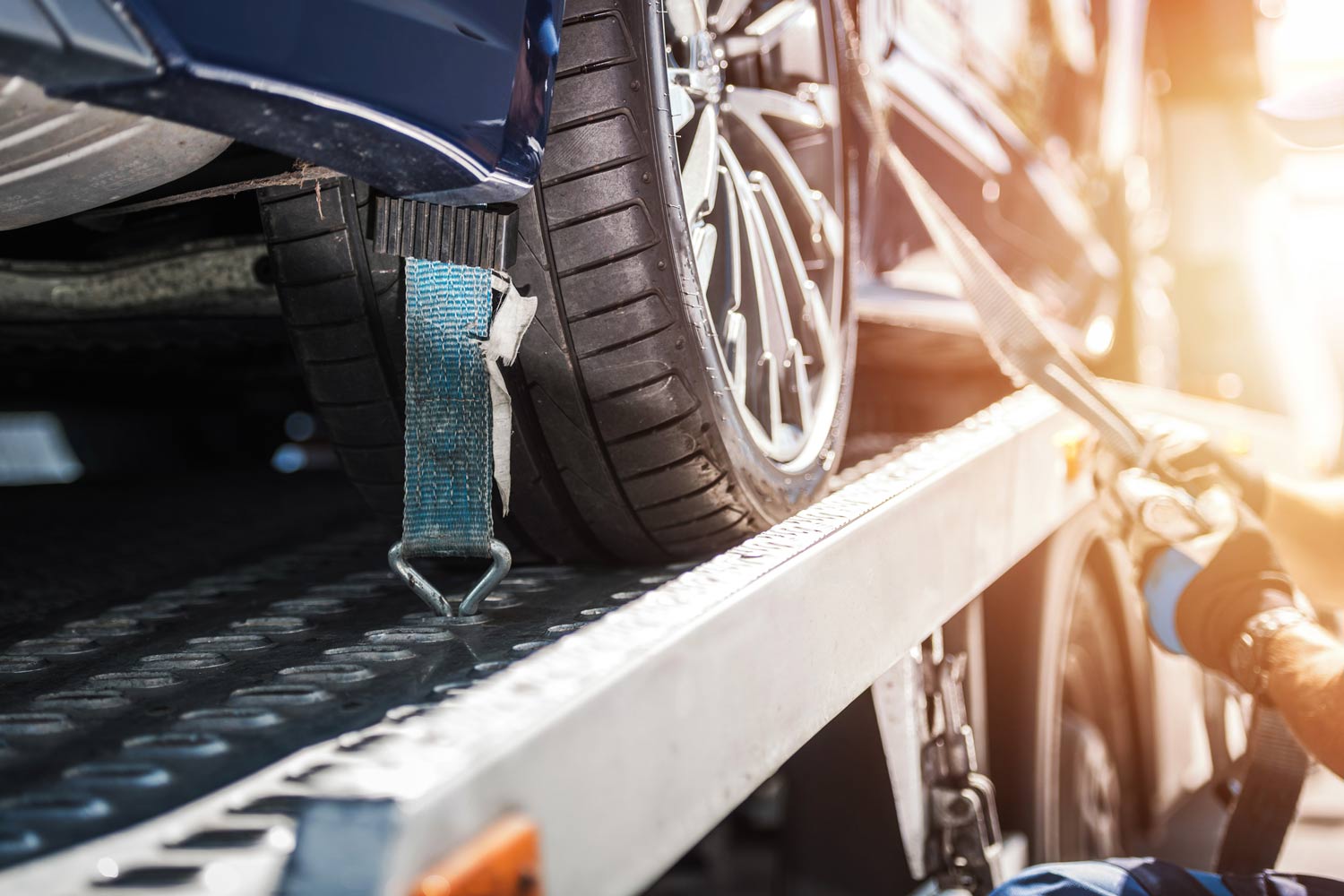 Closeup of a vehicle wheel secured with tie-down straps on a tow truck for safe transport.
