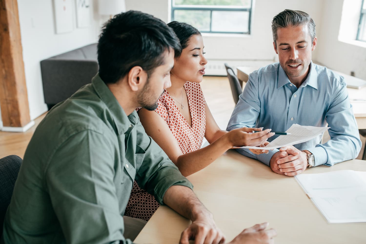 Three people seated in an office, with one person holding a document and discussing it with another.