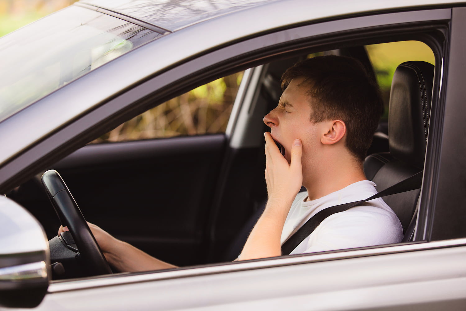 Tired novice driver yawning while driving his car.