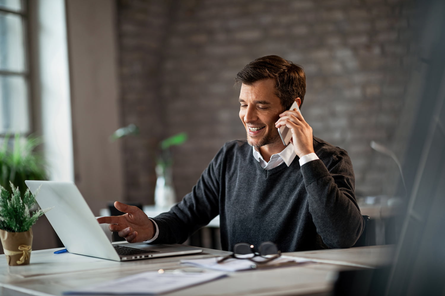Happy man communicating over mobile phone and working on laptop while being at office.