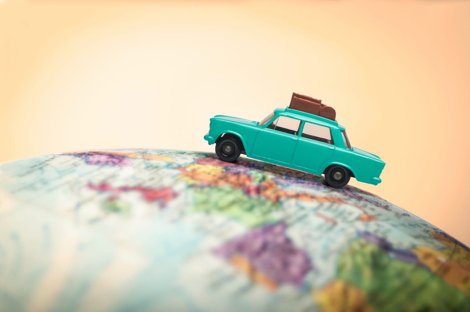 Close-up of a toy car with luggage on holiday sitting on a globe