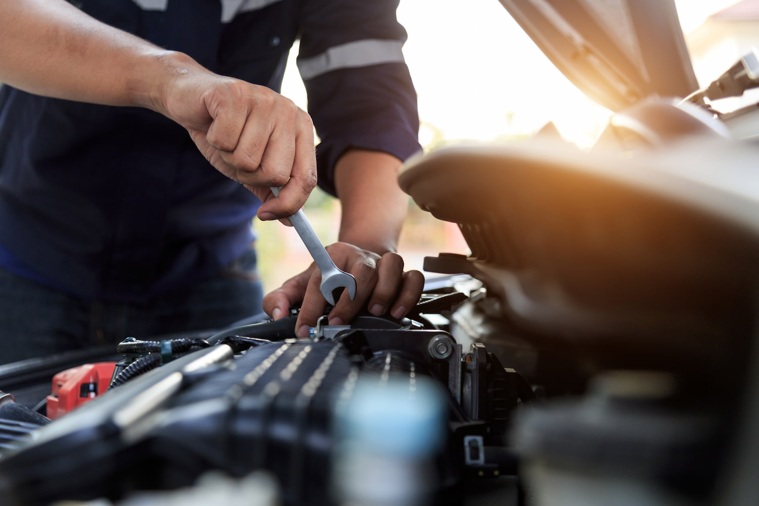 Mechanic working on a car engine with a wrench in an automotive workshop.