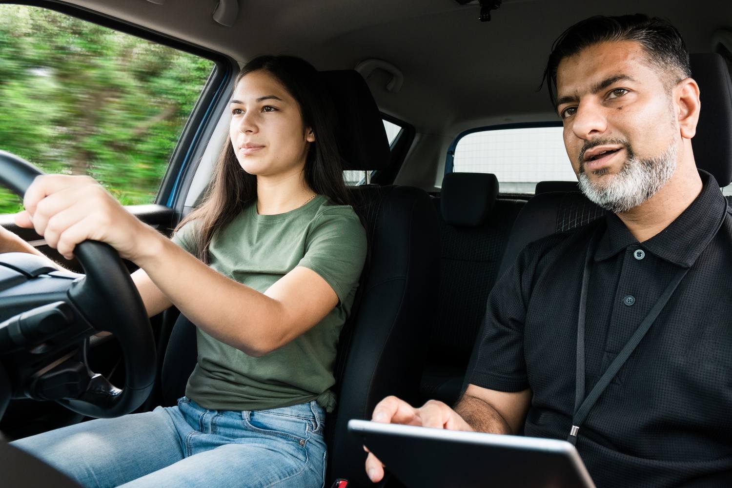 student in passenger seat and instructor in car, holding a clip board.
