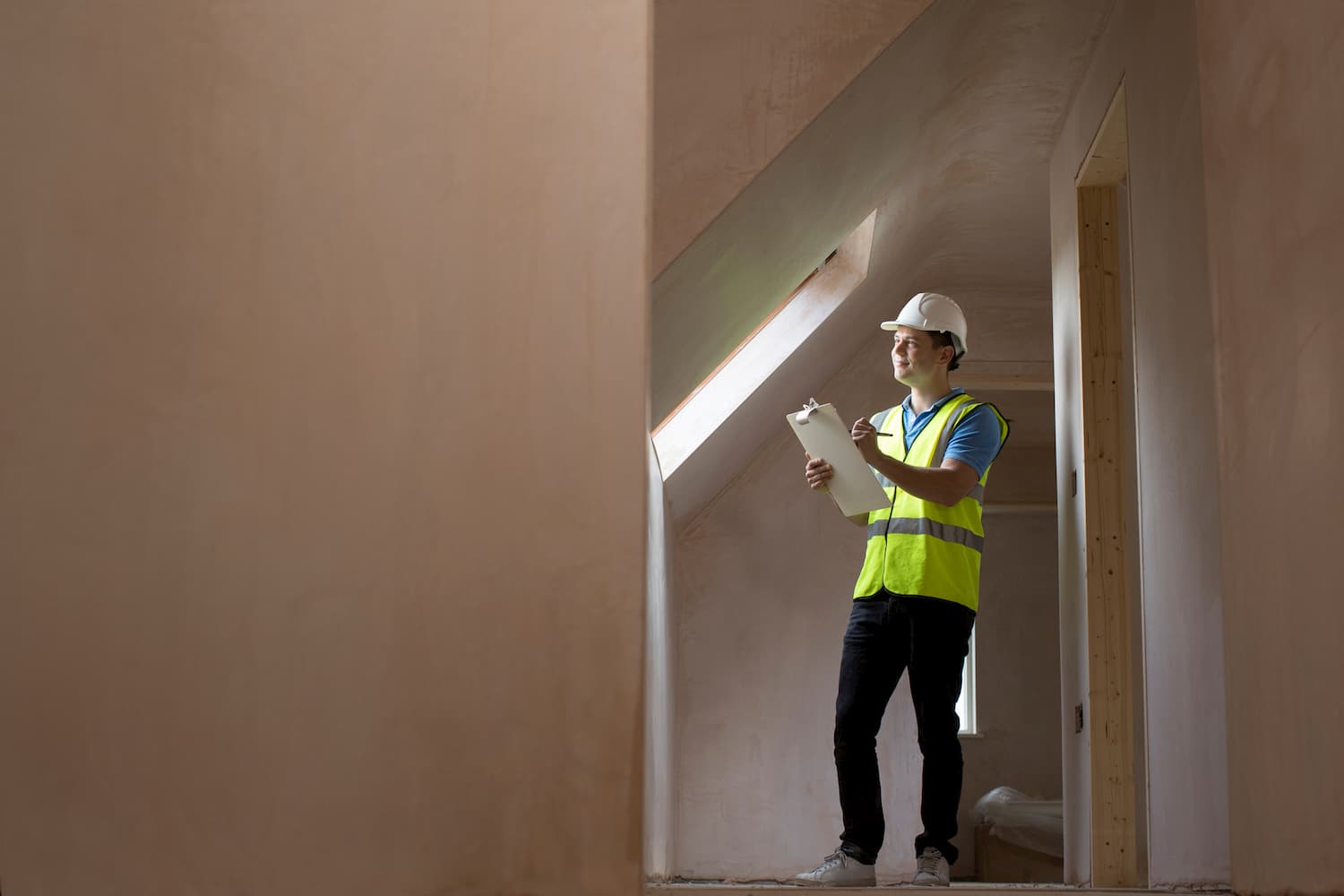 Person wearing a construction hat, holding a clipboard and pen, inspecting a property.
