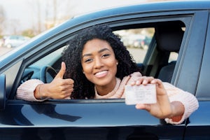 A young smiling woman showing her drive license in a car