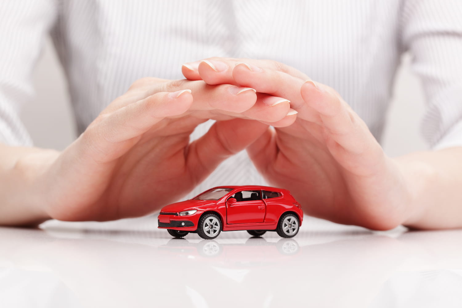 Close up of hands over a red toy car on a white table.