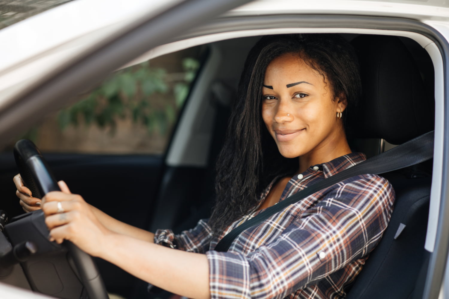A woman seated in the passenger seat of a car, holding the steering wheel and smiling at the camera.
