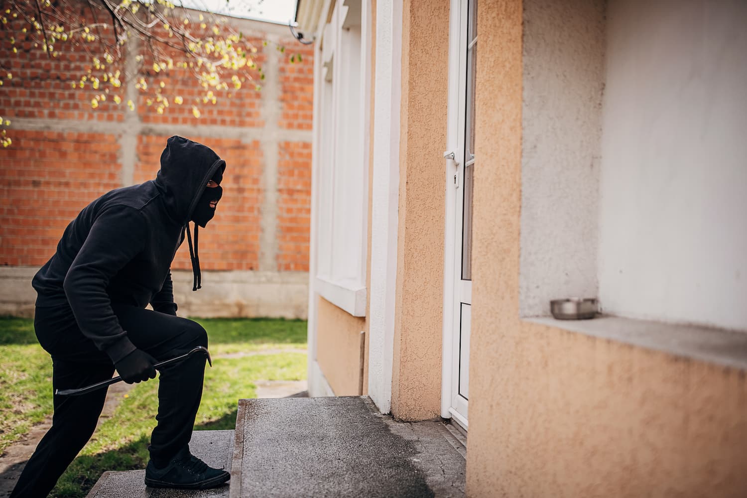 One man, criminal dressed all in black with crowbar, trying to break in house.
