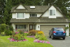 A beautiful home and yard with a garden full of perennials and annuals with a car parked in a driveway