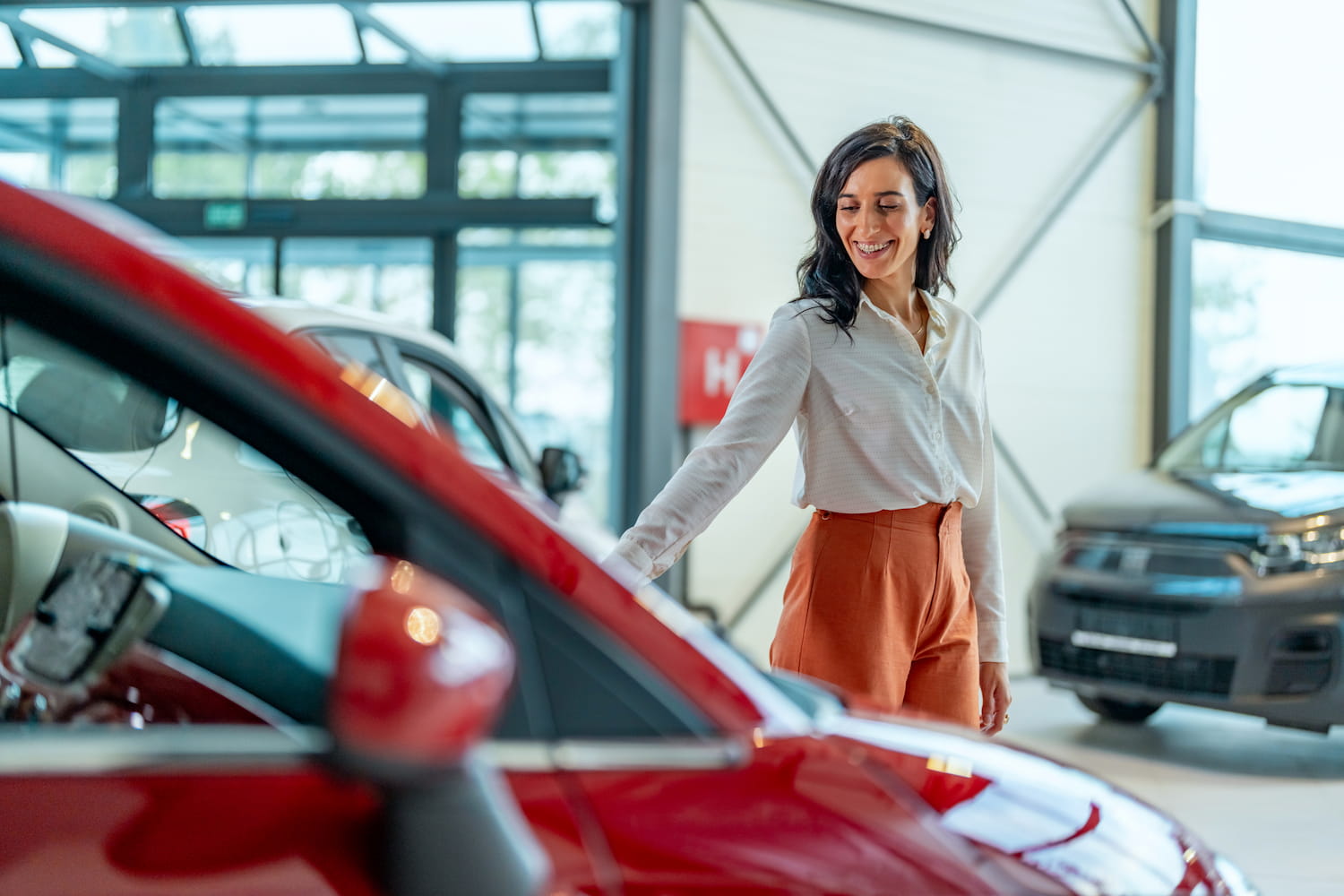 A person standing next to a red car, looking cheerful.