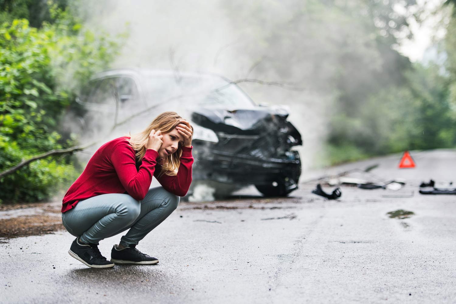 A frustrated person making a phone call next to a damaged car.