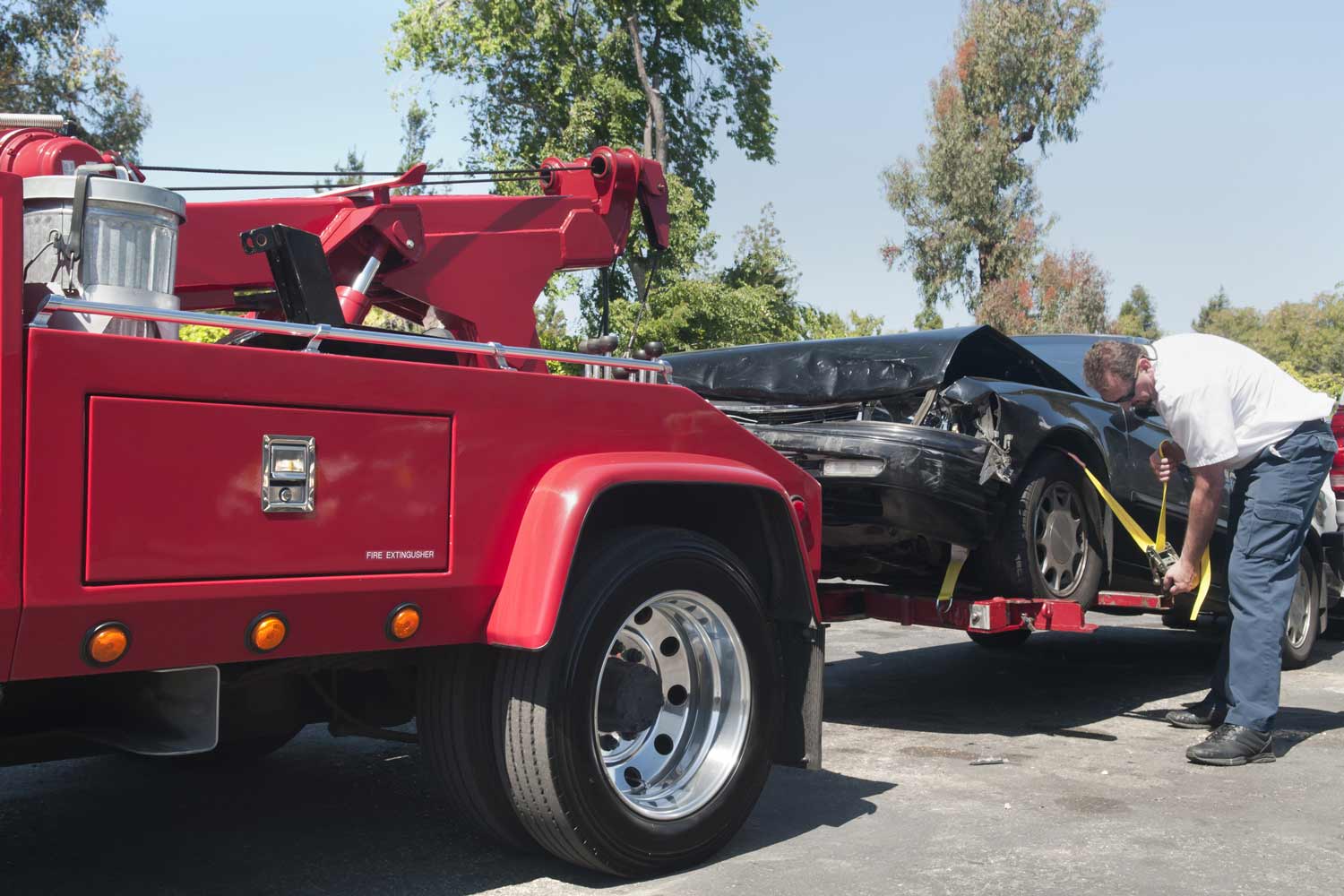A tow truck driver carefully secures a damaged car in preparation for towing.