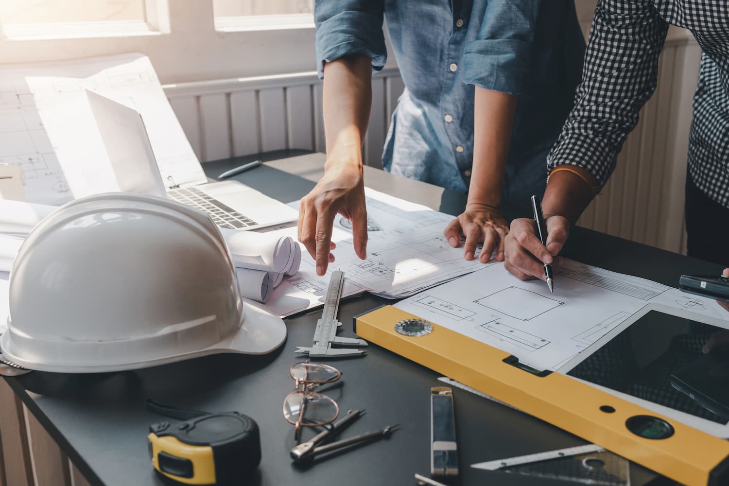 Close-up of architect and engineers holding a pen working on blueprints with safety equipment placed at the office
