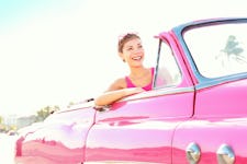 A happy laughing woman sitting in the passenger seat of a retro pink car on a sunny day