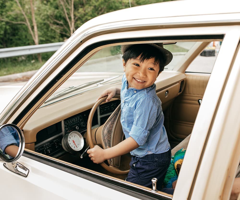 A toddler sitting in the passenger seat of a parked car, smiling at the camera.