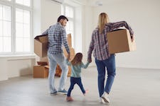 A man and a woman holding their daughter's hands while moving boxes into their new home