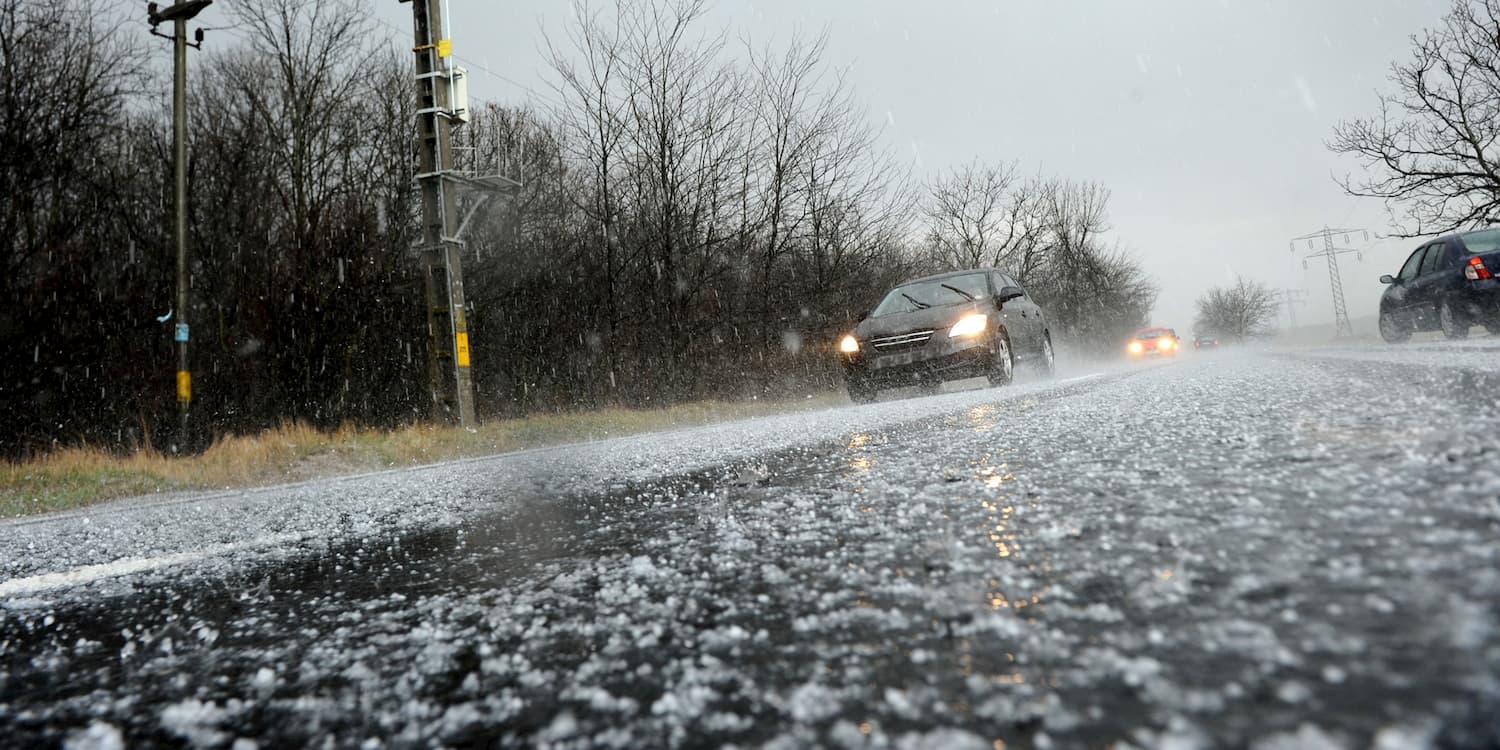 A vehicle travels down a road as hail falls from the sky.
