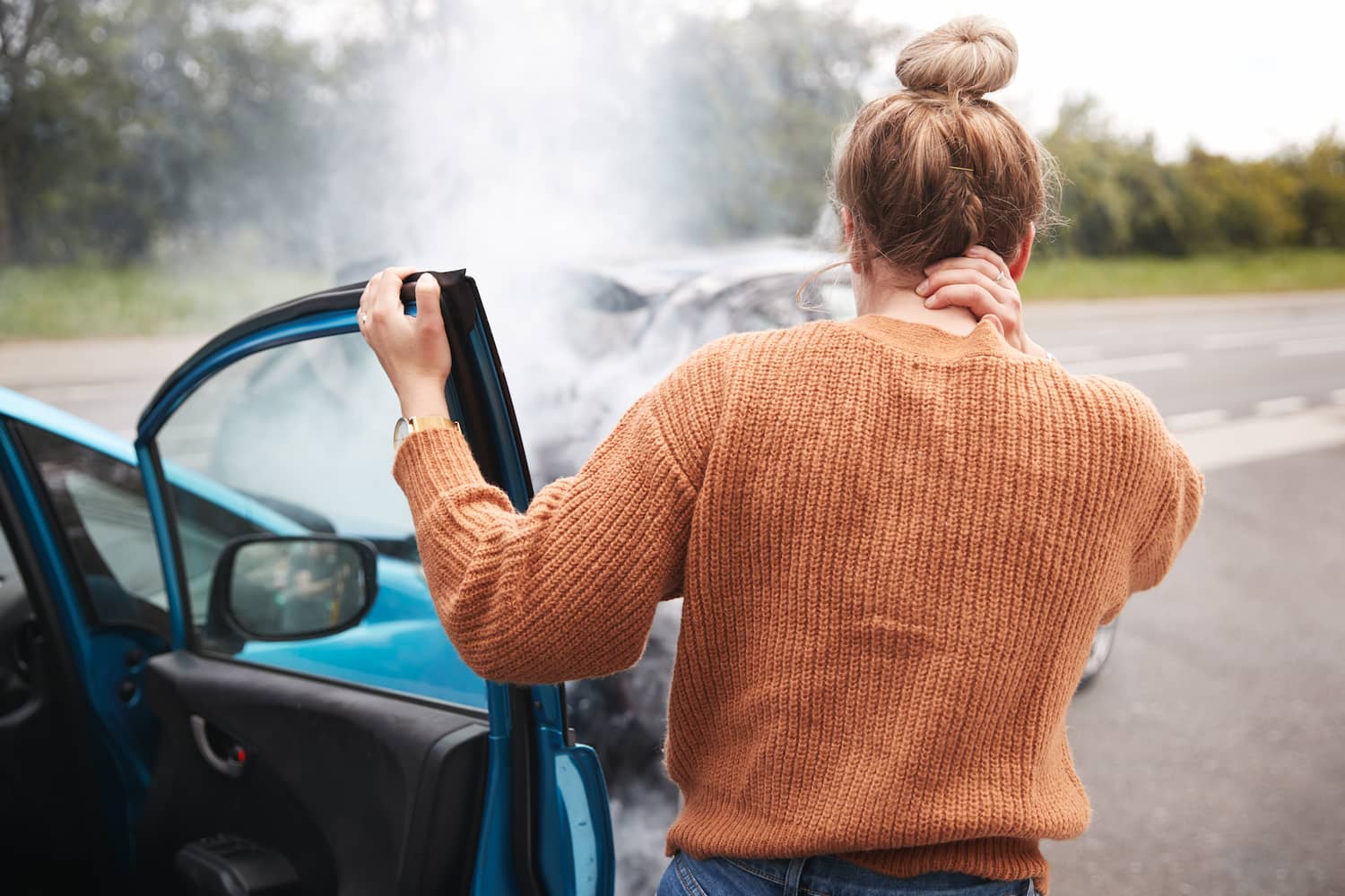 Rear View Of Female Motorist Placing Her Hand Behind Her Neck For What It Seems Like A Head Injury Getting Out Of Car After Crash