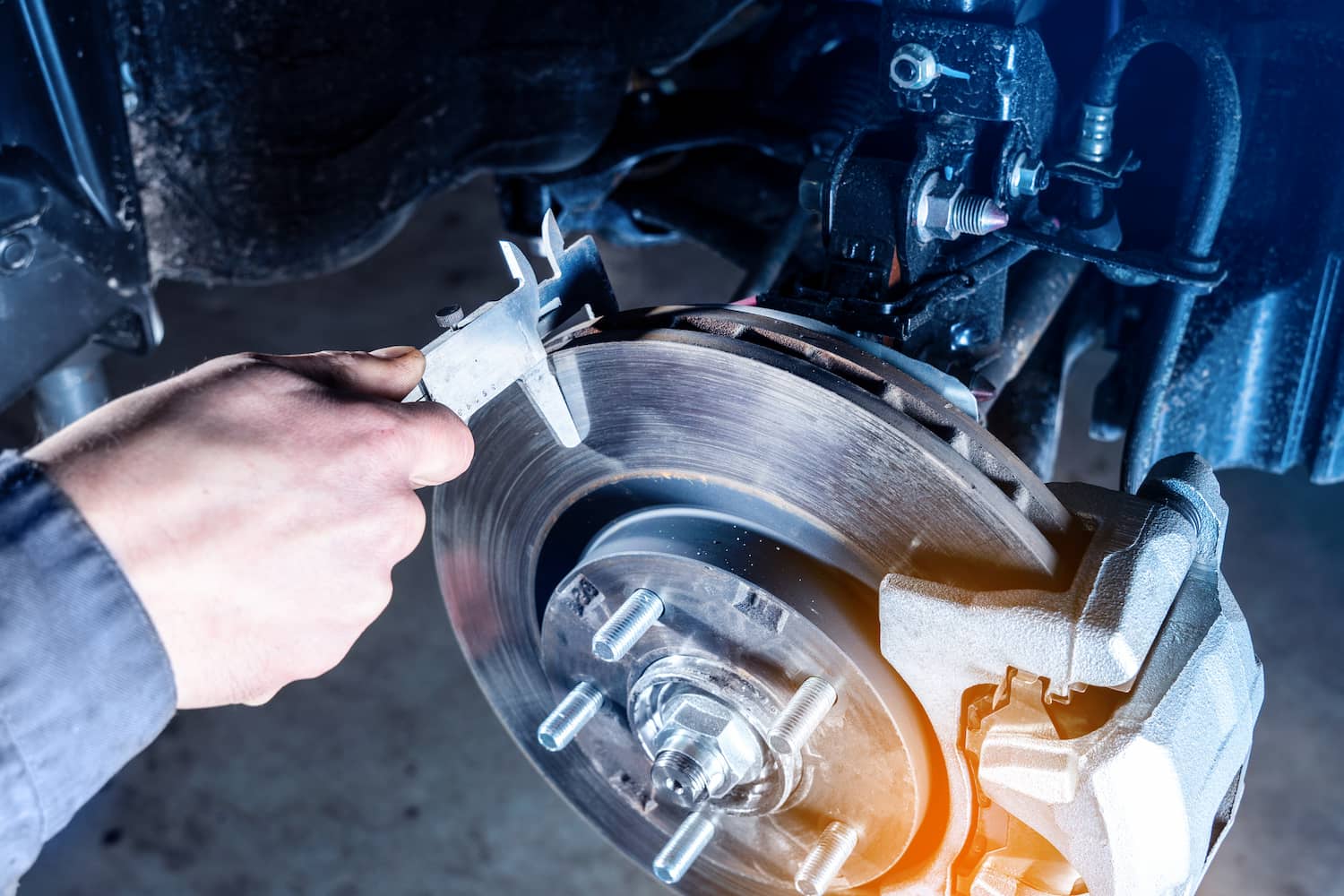 A mechanic's hand checking a car's brake discs wear with calipers.