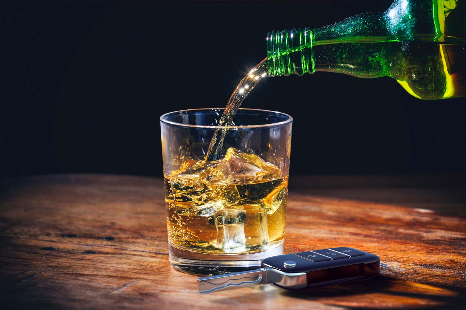 Car key and whiskey glass and bottle on a wooden bar counter background.