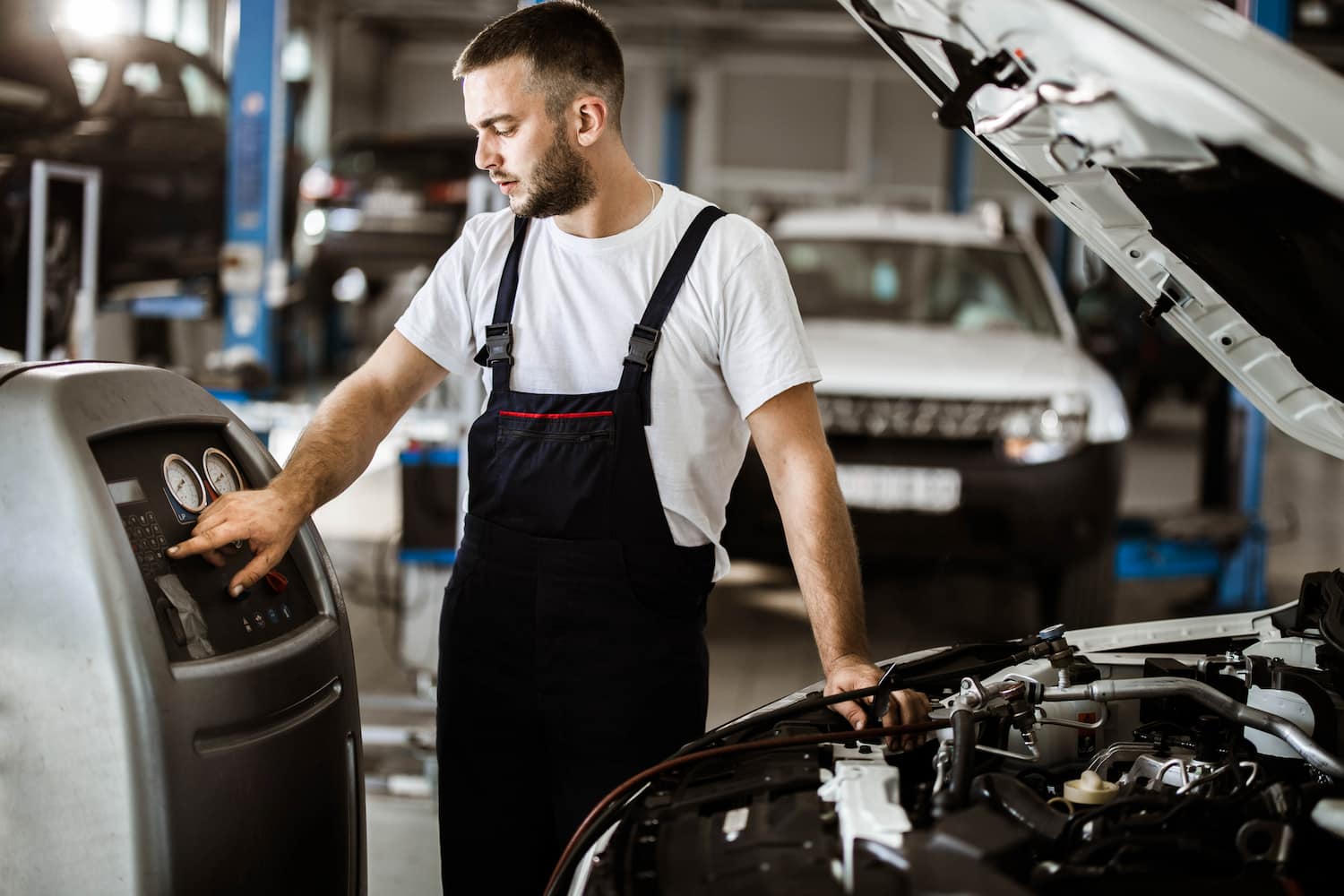 Young auto mechanic refueling car AC in a repair shop.