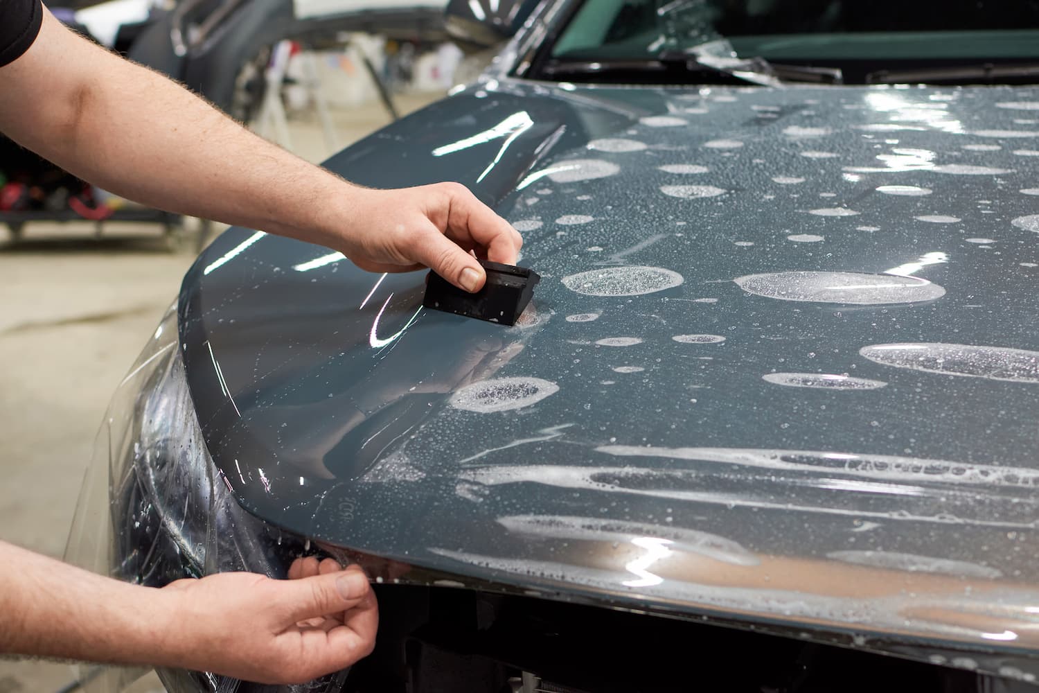 A person applying a clear protective film to a vehicle's surface.