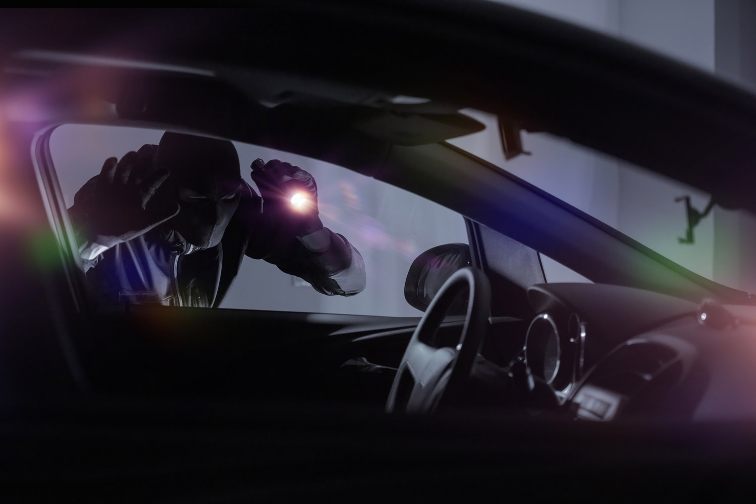 A car thief peering into an empty vehicle while holding a flashlight.