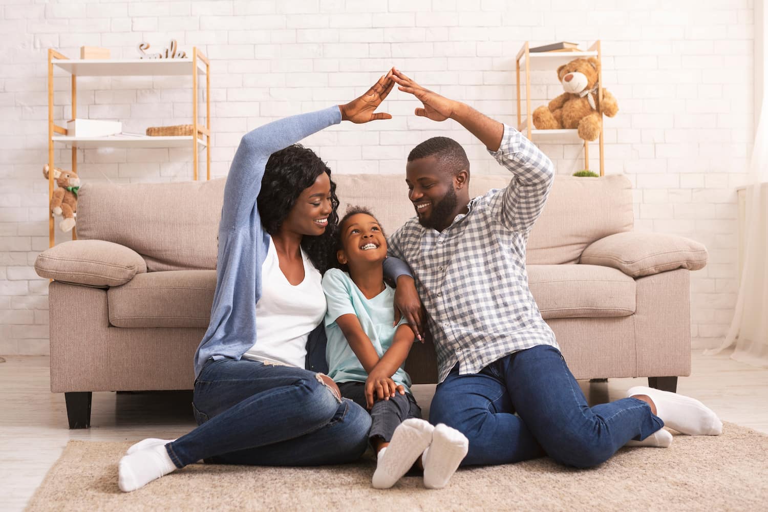 Parents making symbolic roof of hands above their little daughter's head while sitting together on floor at home.