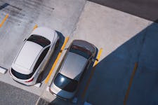 Top view of 2 cars parked on outdoor parking area in front of building with sunlight and shadow on surface