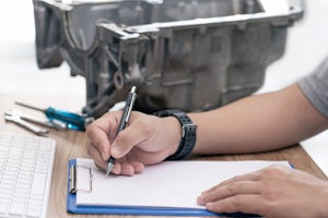 Technician writing on a paper with car oil pan in the background