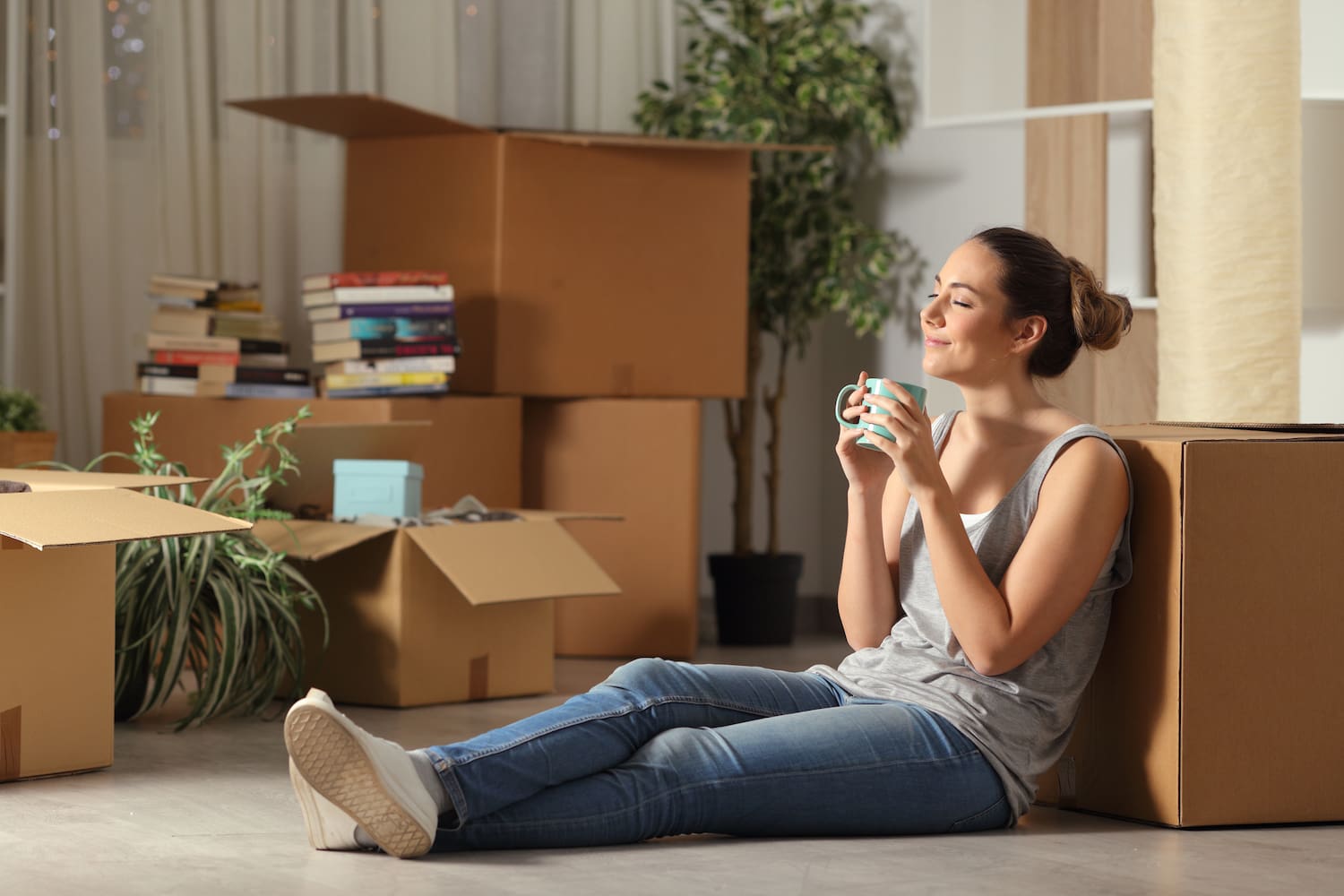 A tenant, smiling, sits on the floor of an apartment while holding a cup.