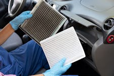 A person setting in a car and holding clean and dirty cabin air filters