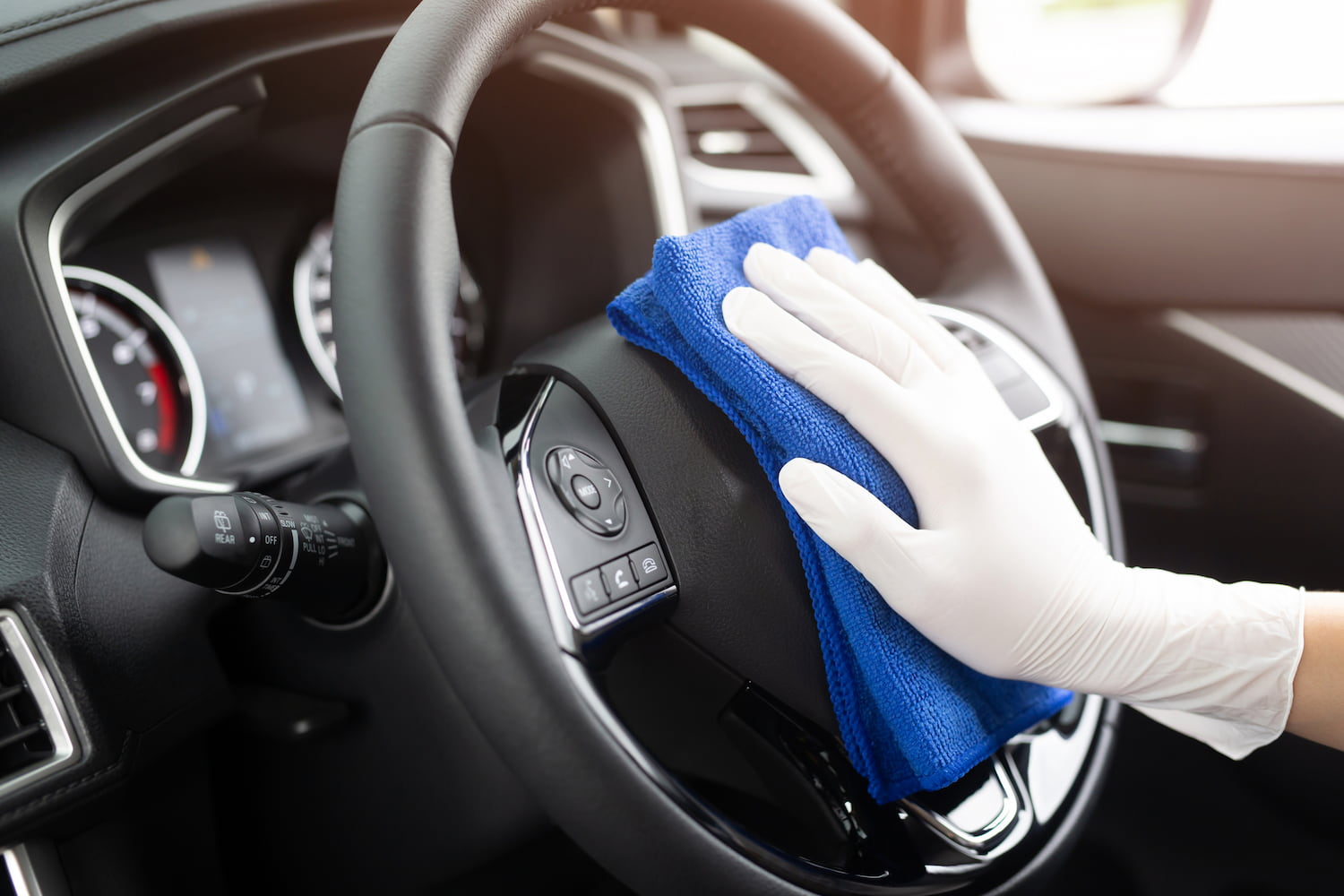 Person is  wearing gloves cleaning car interior console with a blue microfiber cloth.