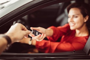 Blurred woman sitting in a car receiving the car keys from a man's hand
